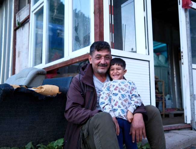 Vader en zoon poseren voor hun containerwoning aan de rand van Antakya. “We waren bang, we dachten dat de bergen achter ons naar beneden zouden komen” 